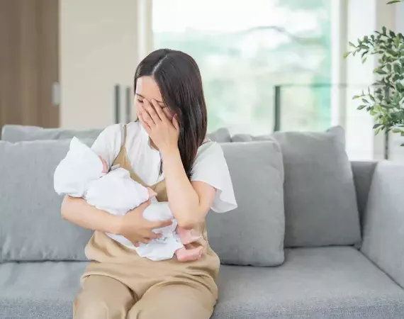 Frau mit kleinem Säugling im Arm auf dem Sofa weint.
